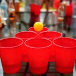 Close-up of red cups and ping pong ball set up for beer pong game at a party.